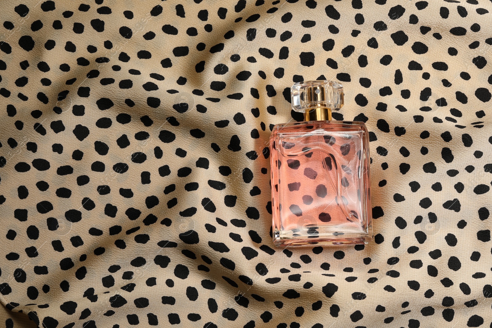 Photo of Luxury perfume in bottle on fabric with leopard pattern, top view