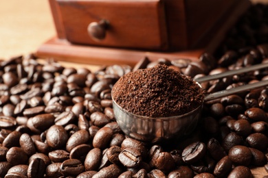 Spoon with coffee grounds and roasted beans on table, closeup