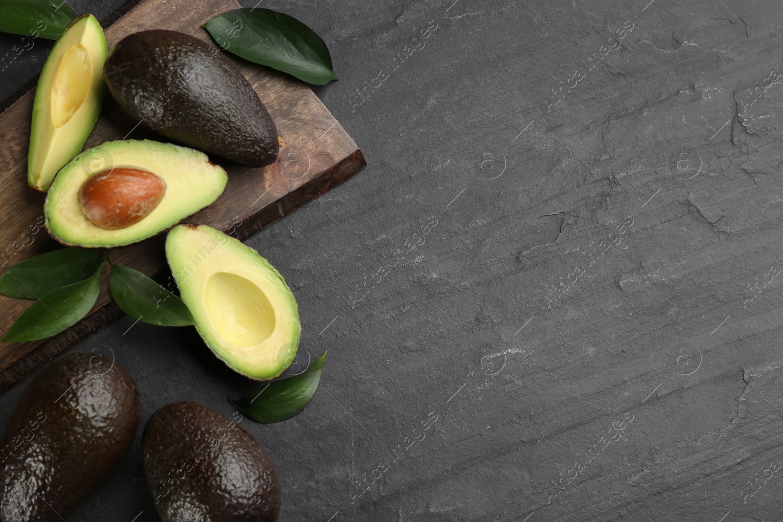 Photo of Whole and cut avocados with green leaves on black table, flat lay. Space for text