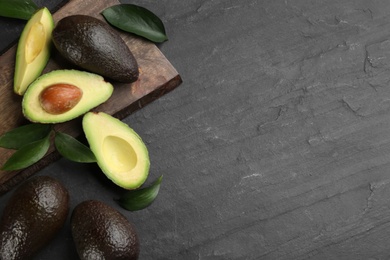 Whole and cut avocados with green leaves on black table, flat lay. Space for text