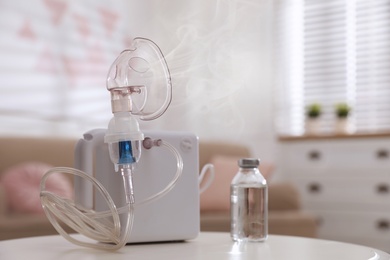 Image of Modern nebulizer with face mask on white table indoors. Inhalation equipment