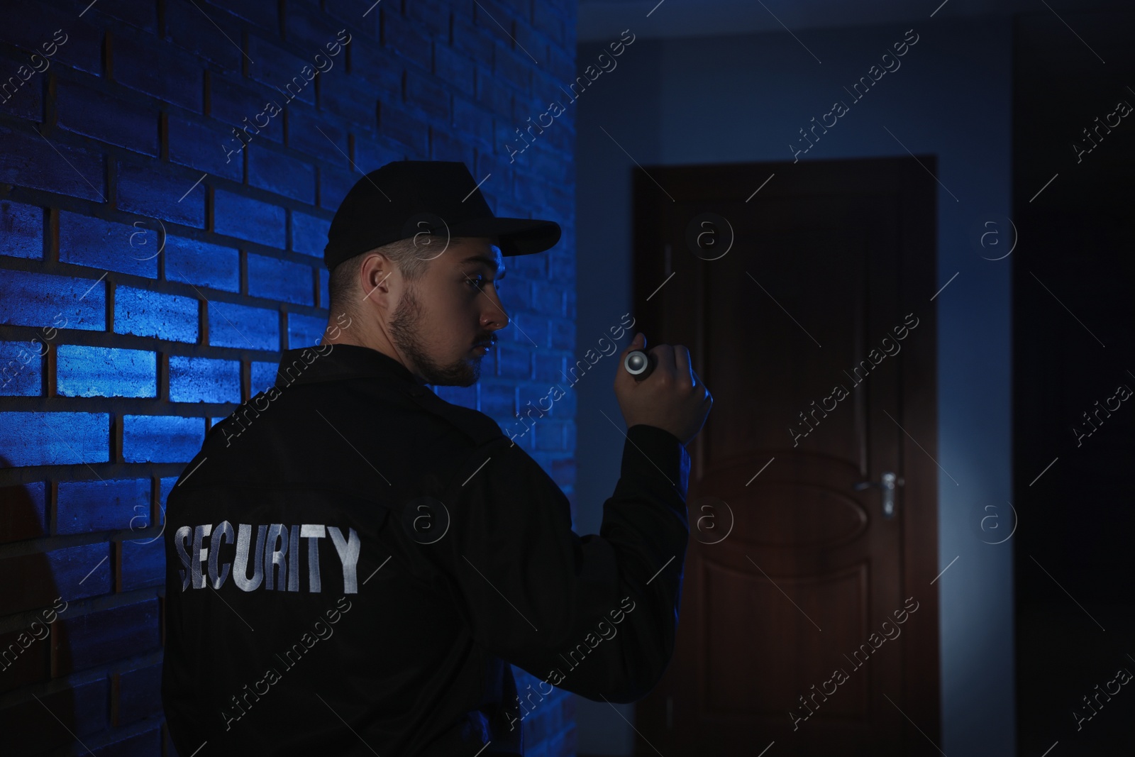 Photo of Male security guard with flashlight in dark corridor