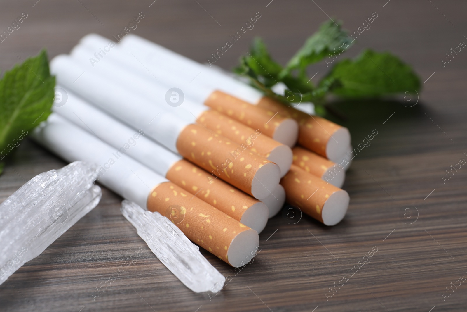 Photo of Cigarettes, menthol crystals and mint on wooden table, closeup