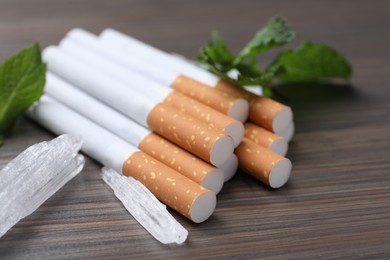 Photo of Cigarettes, menthol crystals and mint on wooden table, closeup