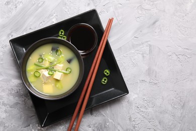 Bowl of delicious miso soup with tofu on light grey table, top view. Space for text