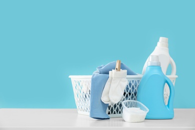 Photo of Detergents and children's clothes on white table near light blue wall. Space for text