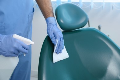 Photo of Professional dentist cleaning workplace with antiseptic in clinic, closeup