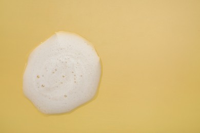 Photo of Spot of white washing foam on yellow background, top view. Space for text