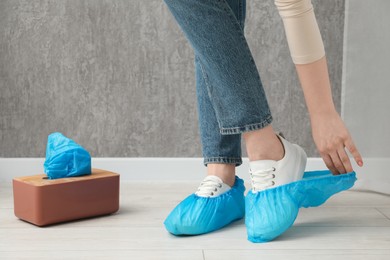 Photo of Woman wearing blue shoe covers onto her sneakers indoors, closeup