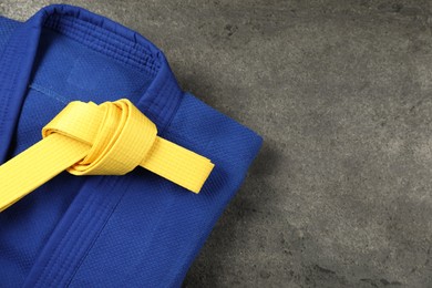 Photo of Yellow karate belt and blue kimono on gray textured background, top view. Space for text