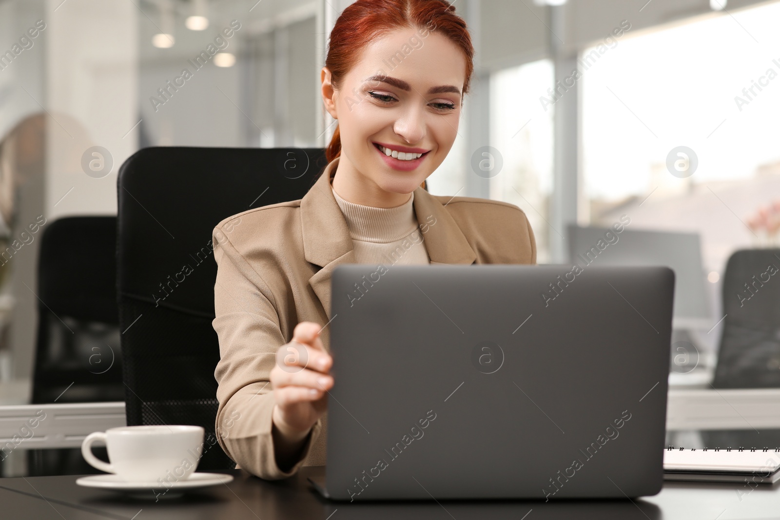 Photo of Happy woman working with laptop at black desk in office