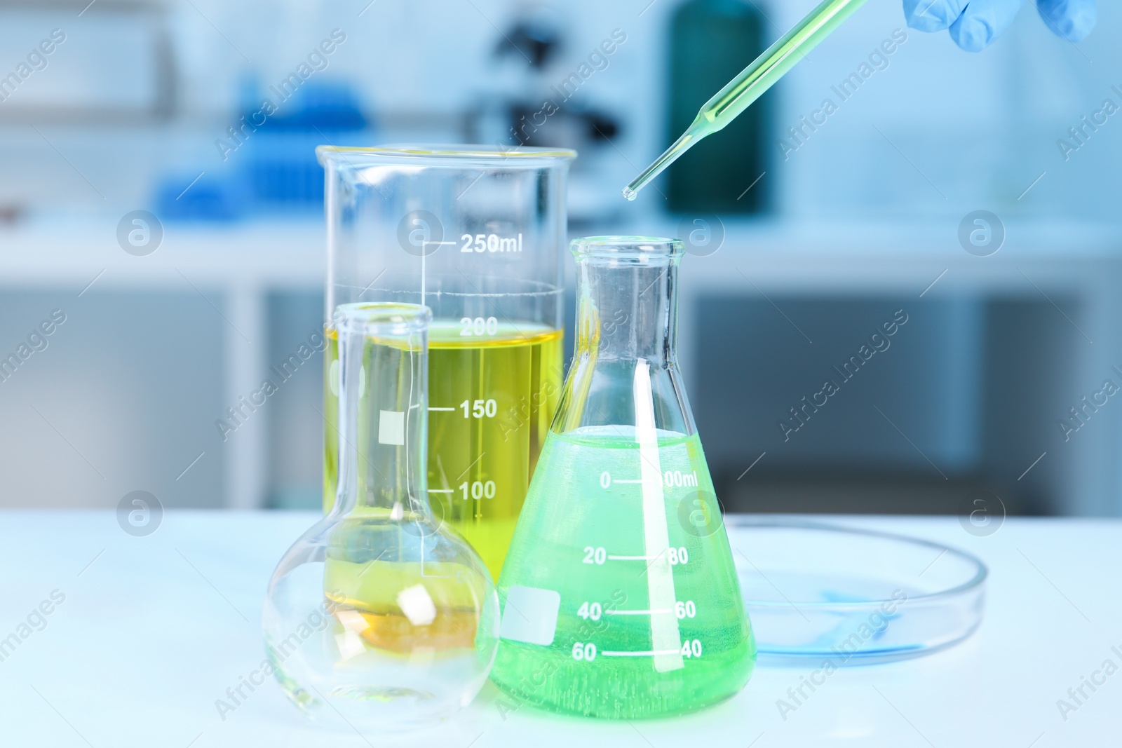 Photo of Laboratory analysis. Woman dripping liquid into flask at white table indoors, closeup