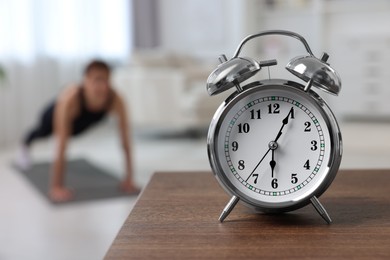 Photo of Morning routine. Alarm clock on wooden table and woman doing exercise, selective focus. Space for text