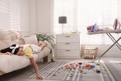 Photo of Tired young mother sleeping on sofa in messy living room