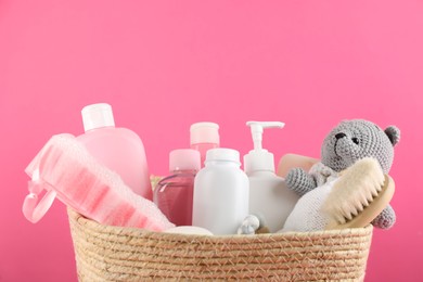 Different baby cosmetic products, bathing accessories and toy in wicker basket on pink background, closeup. Space for text