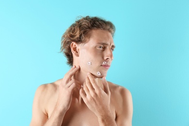 Young man with face hurt while shaving on color background