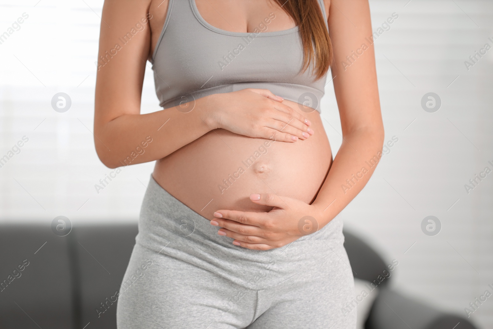 Photo of Pregnant woman standing near sofa at home, closeup