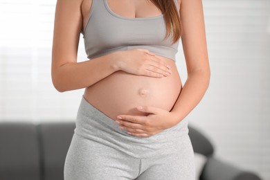 Photo of Pregnant woman standing near sofa at home, closeup