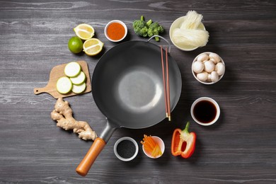 Photo of Empty iron wok and chopsticks surrounded by ingredients on dark grey wooden table, flat lay