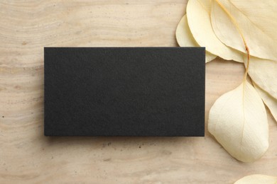Blank business card and beige leaves on wooden table, flat lay. Mockup for design
