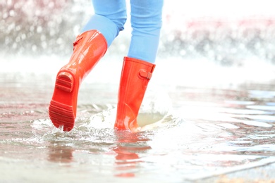 Photo of Woman with red rubber boots in puddle, closeup. Rainy weather