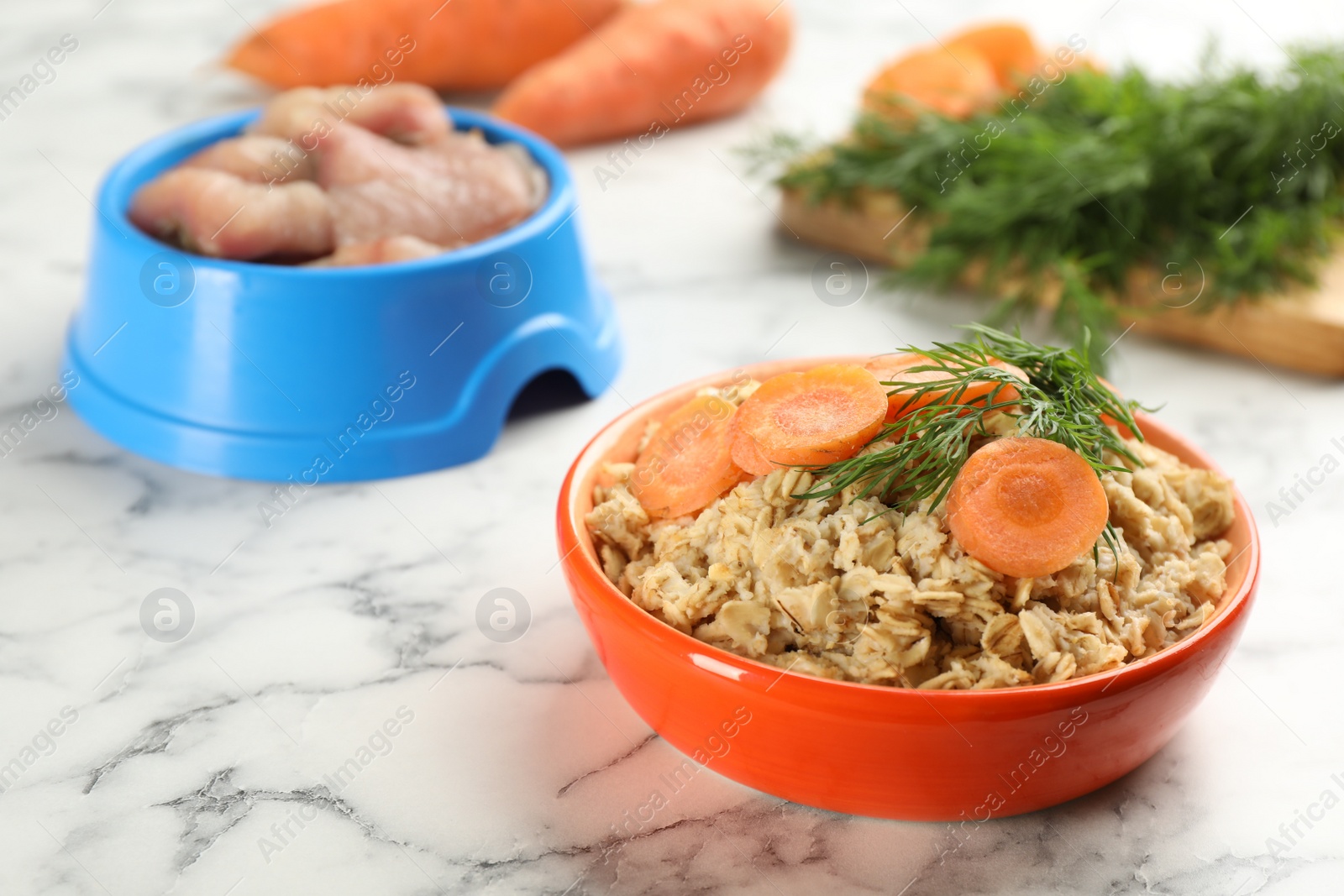 Photo of Natural pet food in feeding bowls on white marble table, closeup