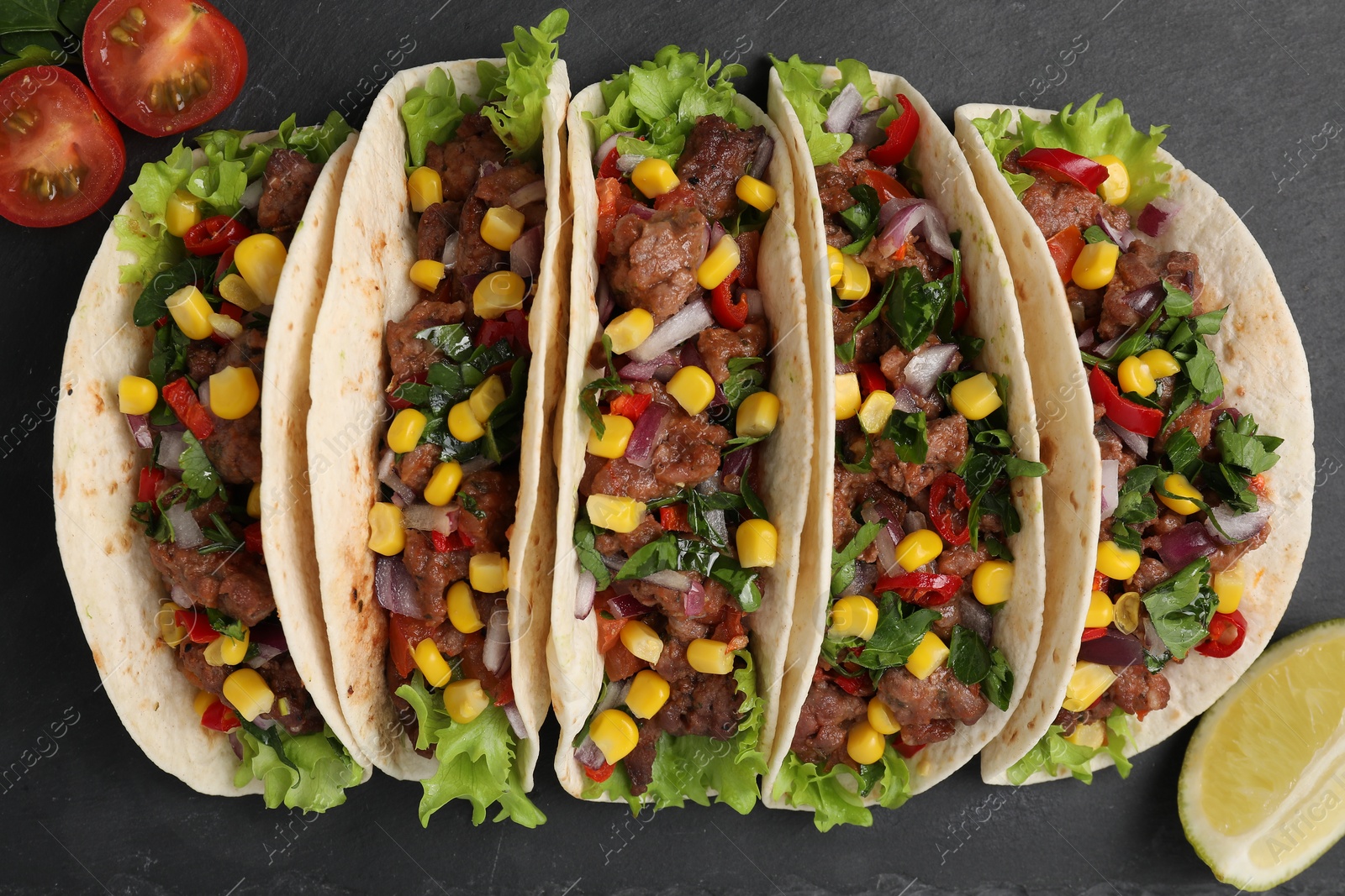 Photo of Delicious tacos with meat, vegetables and lime on dark gray table, flat lay