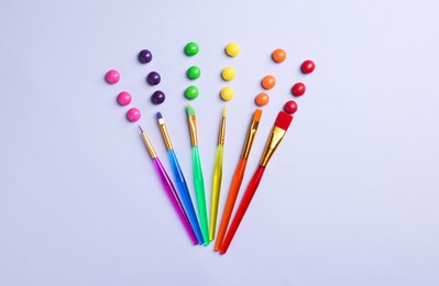 Photo of Creative flat lay composition with paint brushes and colorful candies on light grey background