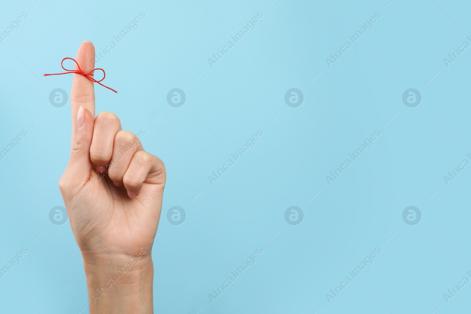 Photo of Woman showing index finger with tied red bow as reminder on light blue background, closeup. Space for text