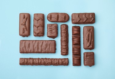 Different tasty chocolate bars on light blue background, flat lay