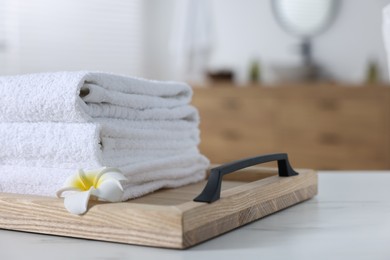 Photo of Wooden tray with stacked bath towels and beautiful flower on white table indoors. Space for text