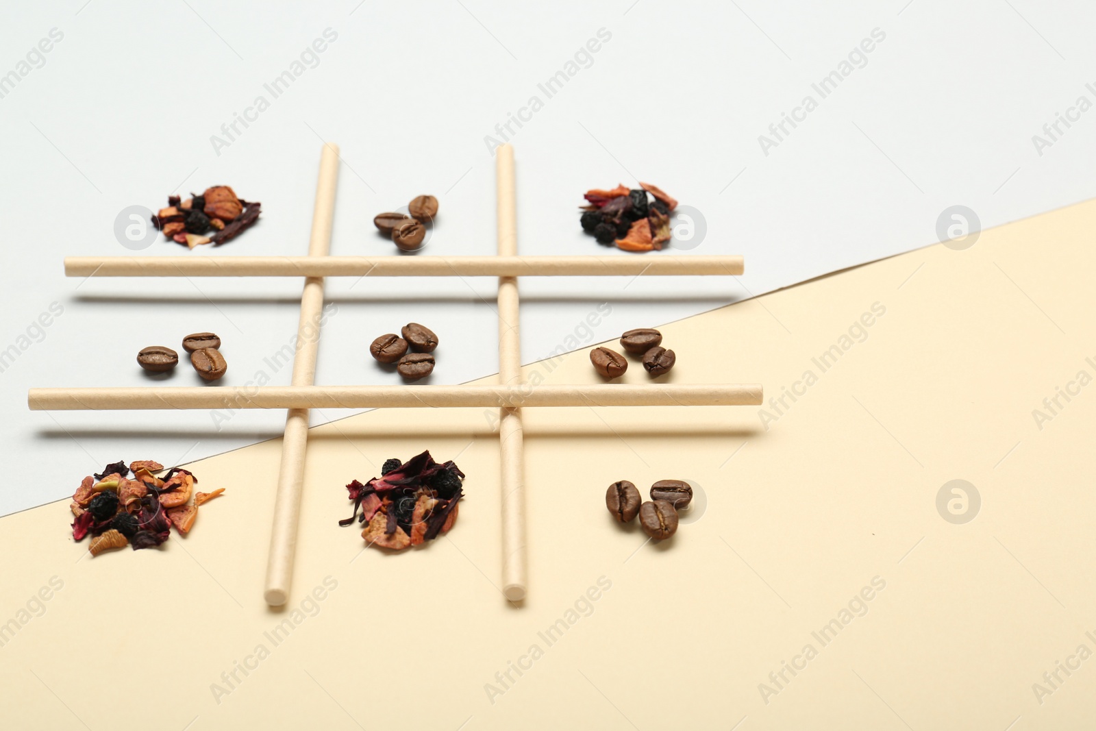 Photo of Tic tac toe game made with coffee beans and dry tea leaves on color background