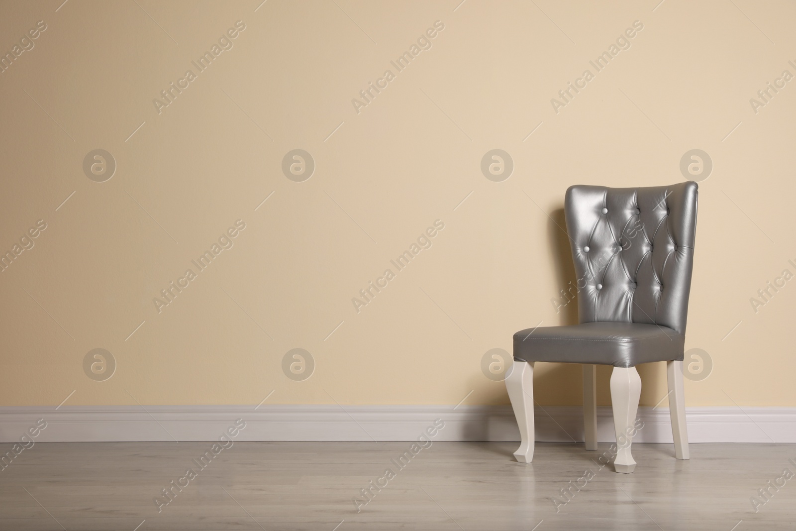 Photo of Stylish silver chair near beige wall. Space for text