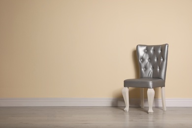 Photo of Stylish silver chair near beige wall. Space for text