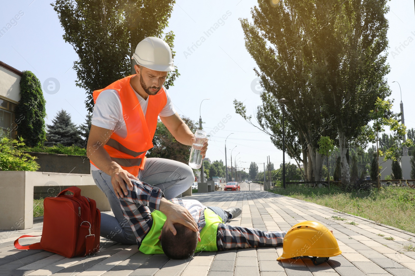 Photo of Worker with bottle of water helping colleague on city street. Suffering from heat stroke