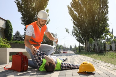 Worker with bottle of water helping colleague on city street. Suffering from heat stroke