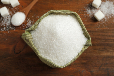 Granulated sugar in sack on wooden table, flat lay