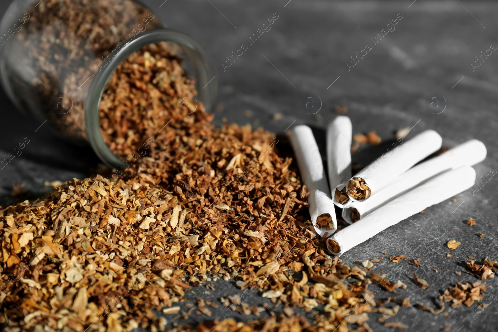 Photo of Tobacco and hand rolled cigarettes on dark grey table, closeup