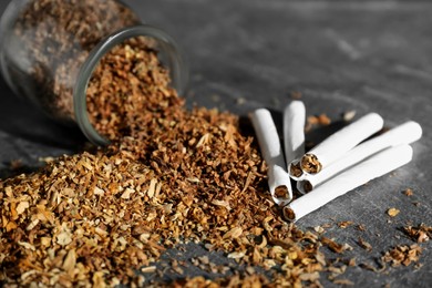 Photo of Tobacco and hand rolled cigarettes on dark grey table, closeup