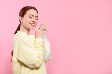 Photo of Woman popping bubble wrap on pink background, space for text. Stress relief