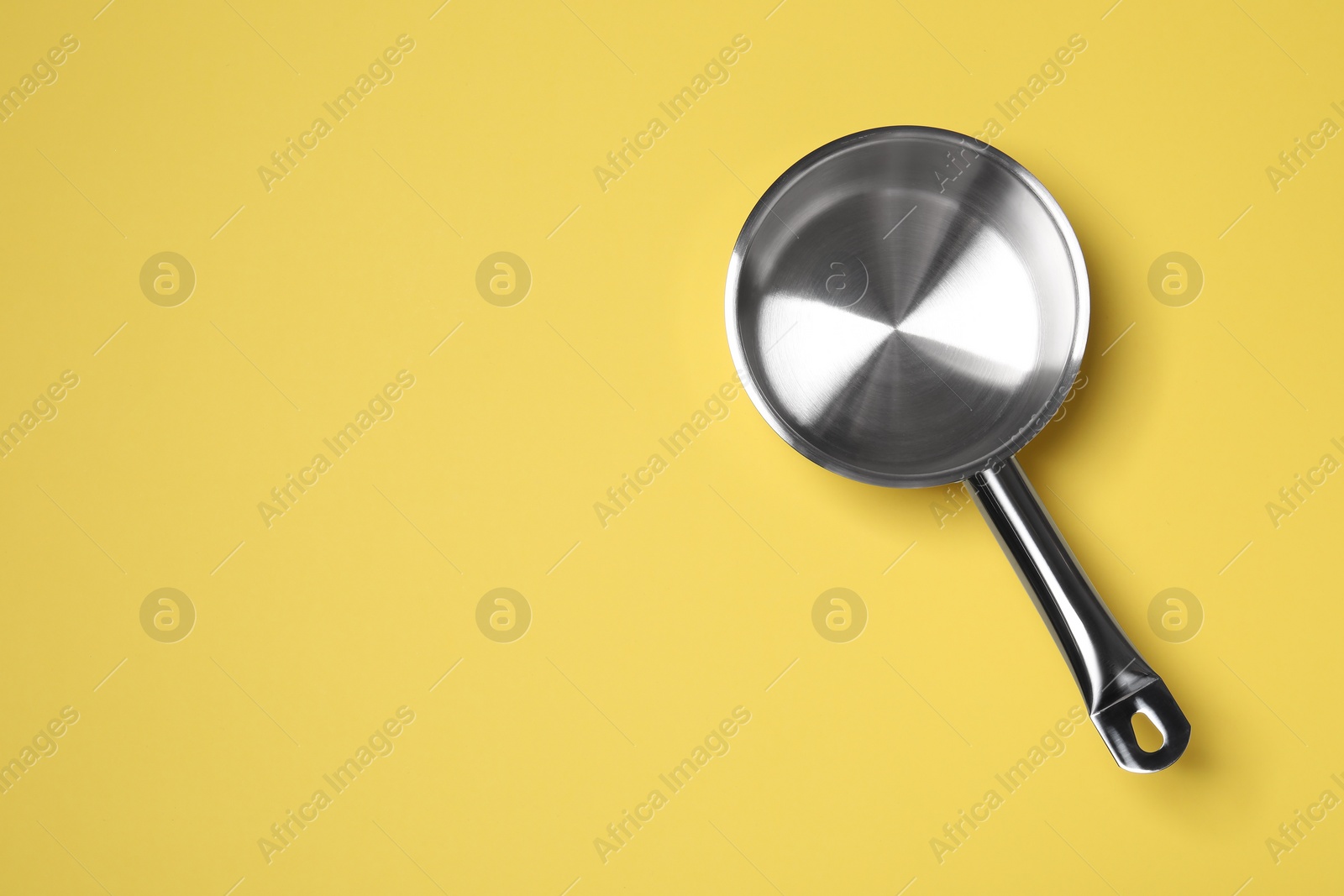 Photo of Empty steel saucepan on yellow background, top view. Space for text