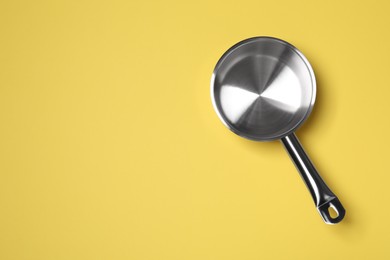 Empty steel saucepan on yellow background, top view. Space for text