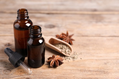 Bottles of essential oil, anise and seeds on wooden table. Space for text