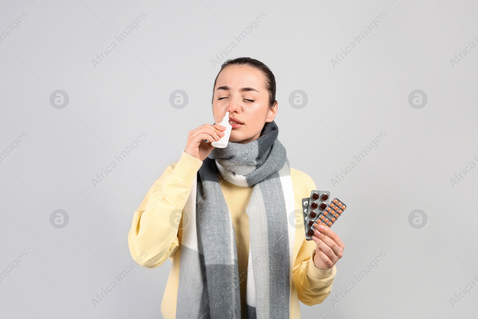 Photo of Woman with pills using nasal spray on light grey background