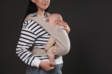 Mother holding her child in baby carrier on black background, closeup. Space for text