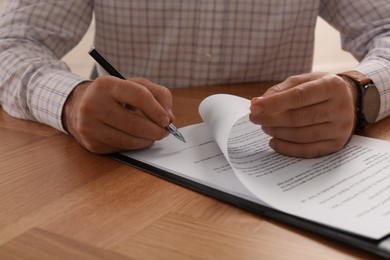 Businessman signing contract at wooden table, closeup of hands