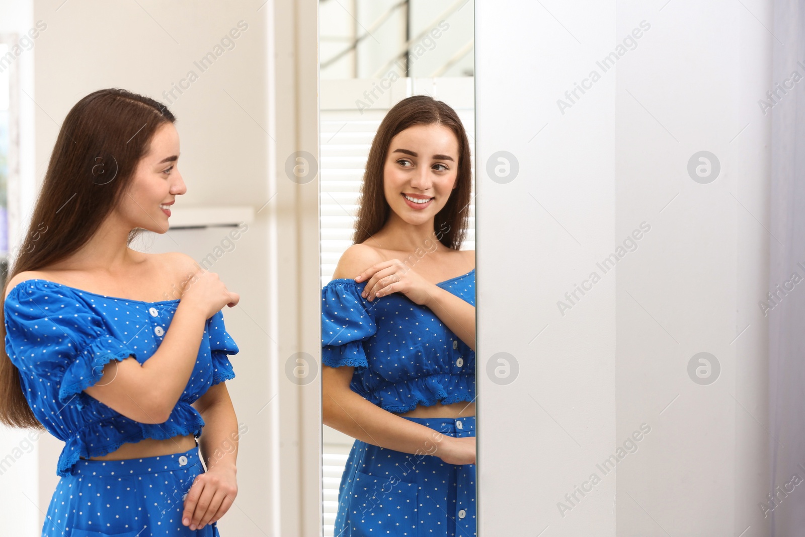 Photo of Beautiful young woman looking at herself in large mirror indoors