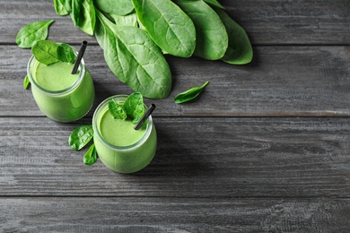 Jars of healthy green smoothie with fresh spinach on grey wooden table, above view. Space for text