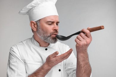 Chef in uniform tasting something on grey background