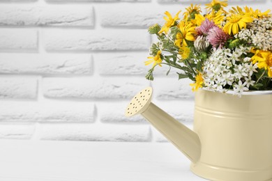 Photo of Beautiful bouquet of bright wildflowers in watering can on white wooden table near brick wall, closeup. Space for text